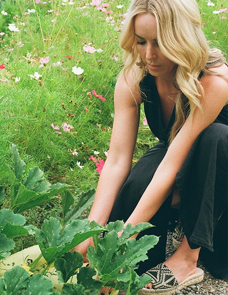 A Woman Kneels to Pick Up a Small Plant From the Ground, Focusing Intently on Her Task.